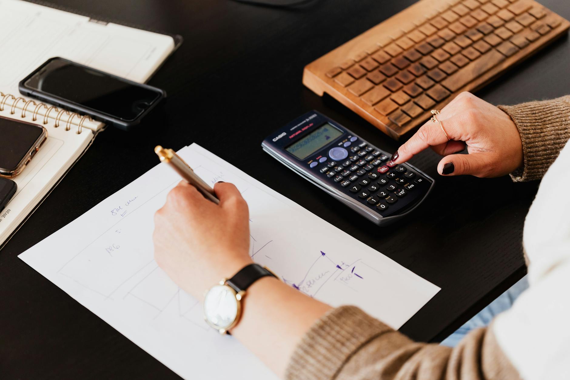 bookkeeper writing down on paper while using calculator